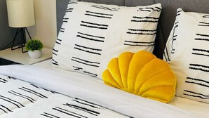 A bed with white bedding and black stripes, a yellow accent pillow, and a grey headboard.