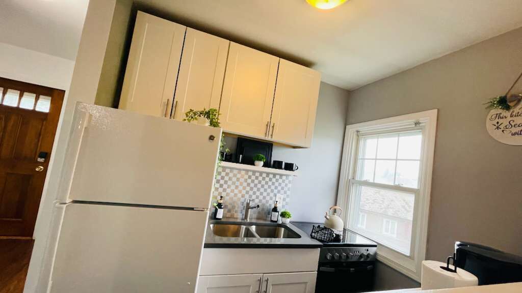 A kitchen with white cabinets, a refrigerator, a sink, and a window.