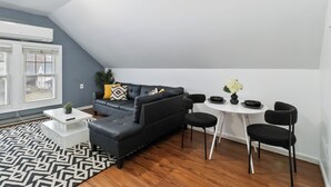 A modern living room with a black sectional sofa, a white coffee table, a dining table with black chairs, and a patterned rug.