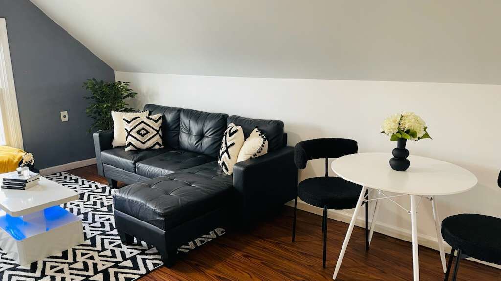A modern living room with a black leather sofa, a white round table, and black chairs.