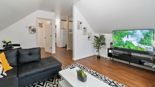 A modern living room with a black leather sofa, a white coffee table, and a large flat-screen TV displaying a nature scene.