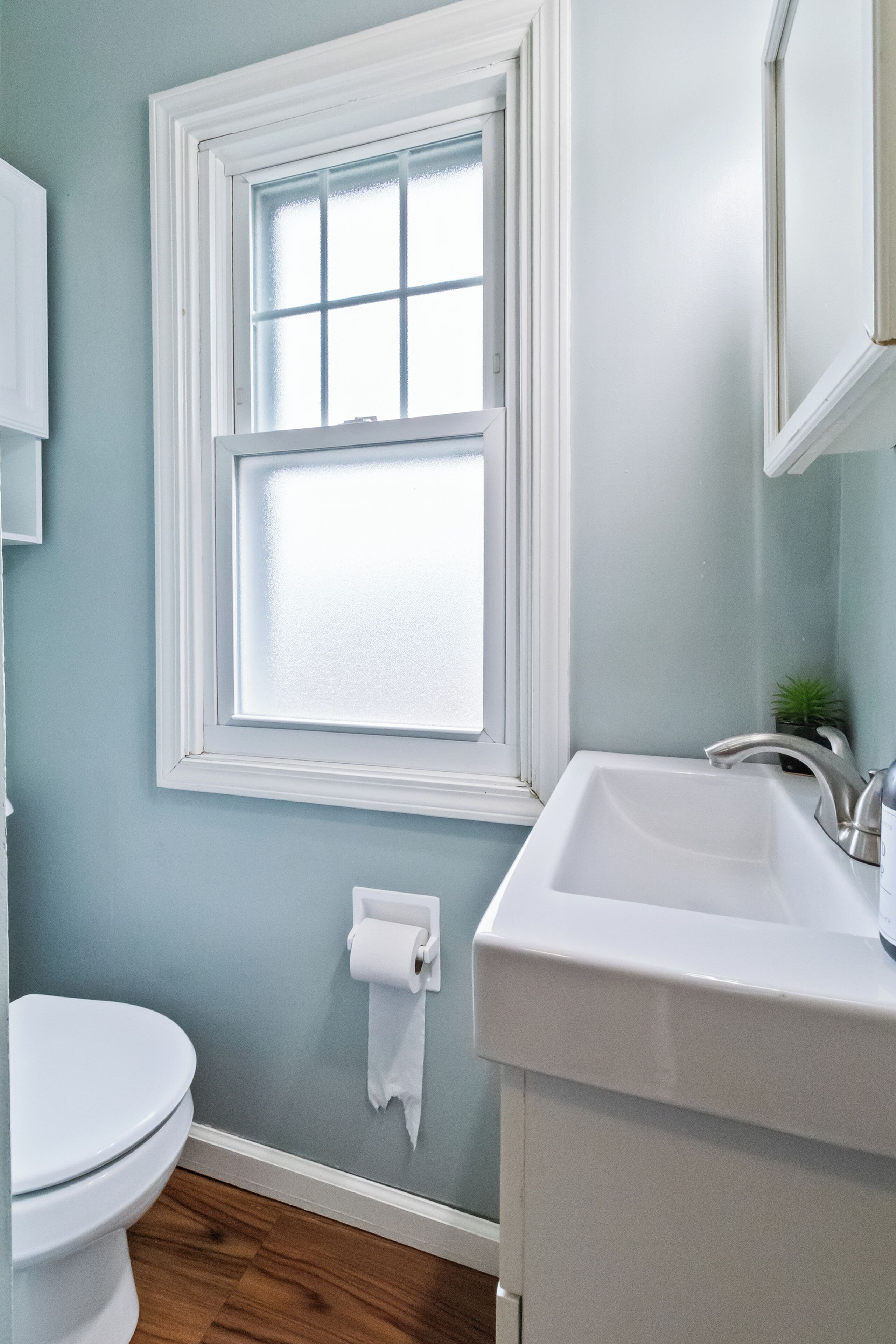 A bathroom with a toilet, a sink, a window, and a roll of toilet paper on the wall.