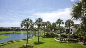A landscaped area with a pond, palm trees, and a building in the background. - Gold-rated 2 bed/2 bath condo with view of the lagoon, just steps to the pool. (Saint Augustine)