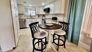 A compact kitchen with white cabinets, a microwave, and a dining area with a round table and two chairs. - Awesome condo, steps to the heated indoor/outdoor pool, short walk to the beach! (Saint Augustine)