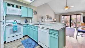 A modern kitchen with teal cabinets, white appliances, and a large window overlooking a balcony. - Great property perfect for a couples getaway to the beach, steps to pool & sand! (Saint Augustine)