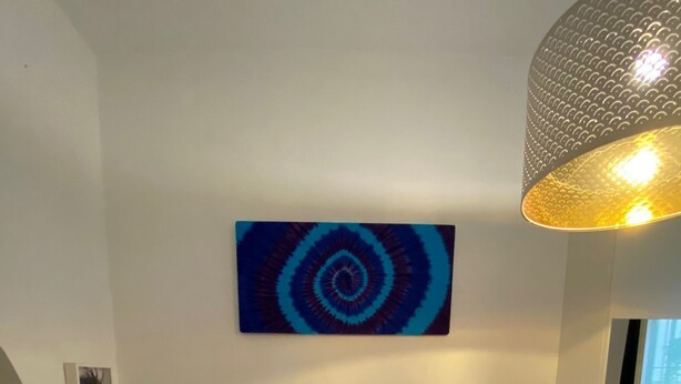 A modern bedroom with a large bed, two blue pillows, a white headboard, a wall-mounted abstract painting, a bedside table with a lamp, and a small nightstand. - 1 Bedroom Apartment in Salerno (Salerno)