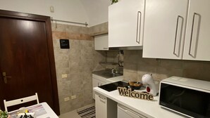 A compact kitchen with white cabinets, a microwave, and a sink. There's a 'Welcome' sign on the counter. - 1 Bedroom Apartment in Salerno (Salerno)
