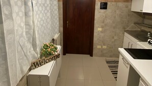 A modern kitchen with a wooden door, white cabinets, a welcome sign, and a pendant light. - 1 Bedroom Apartment in Salerno (Salerno)