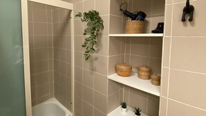 A bathroom with beige tiles, a shower enclosure, a toilet, and shelves with baskets and a plant. - 1 Bedroom Apartment in Salerno (Salerno)