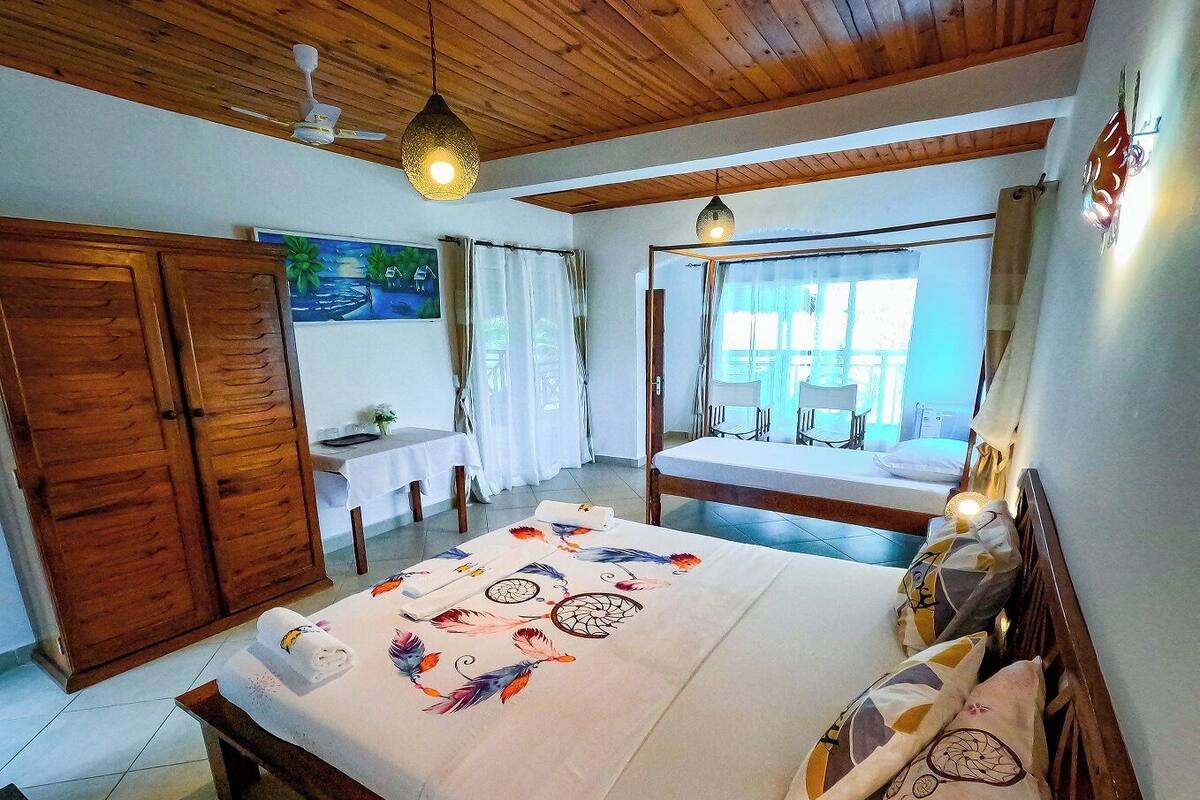 A bedroom with a wooden ceiling, a bed with a floral bedspread, a desk with a chair, and a window with curtains.