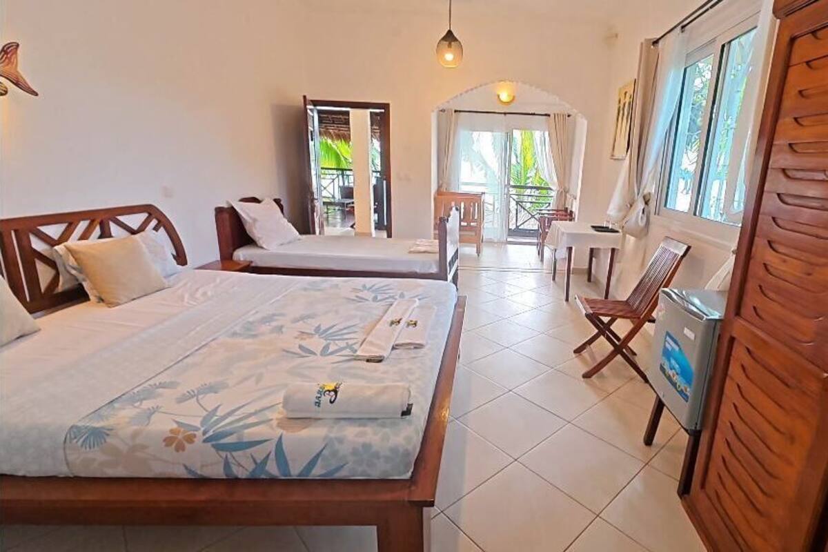 A hotel room with two beds, a dining area, and a view of the outdoors.