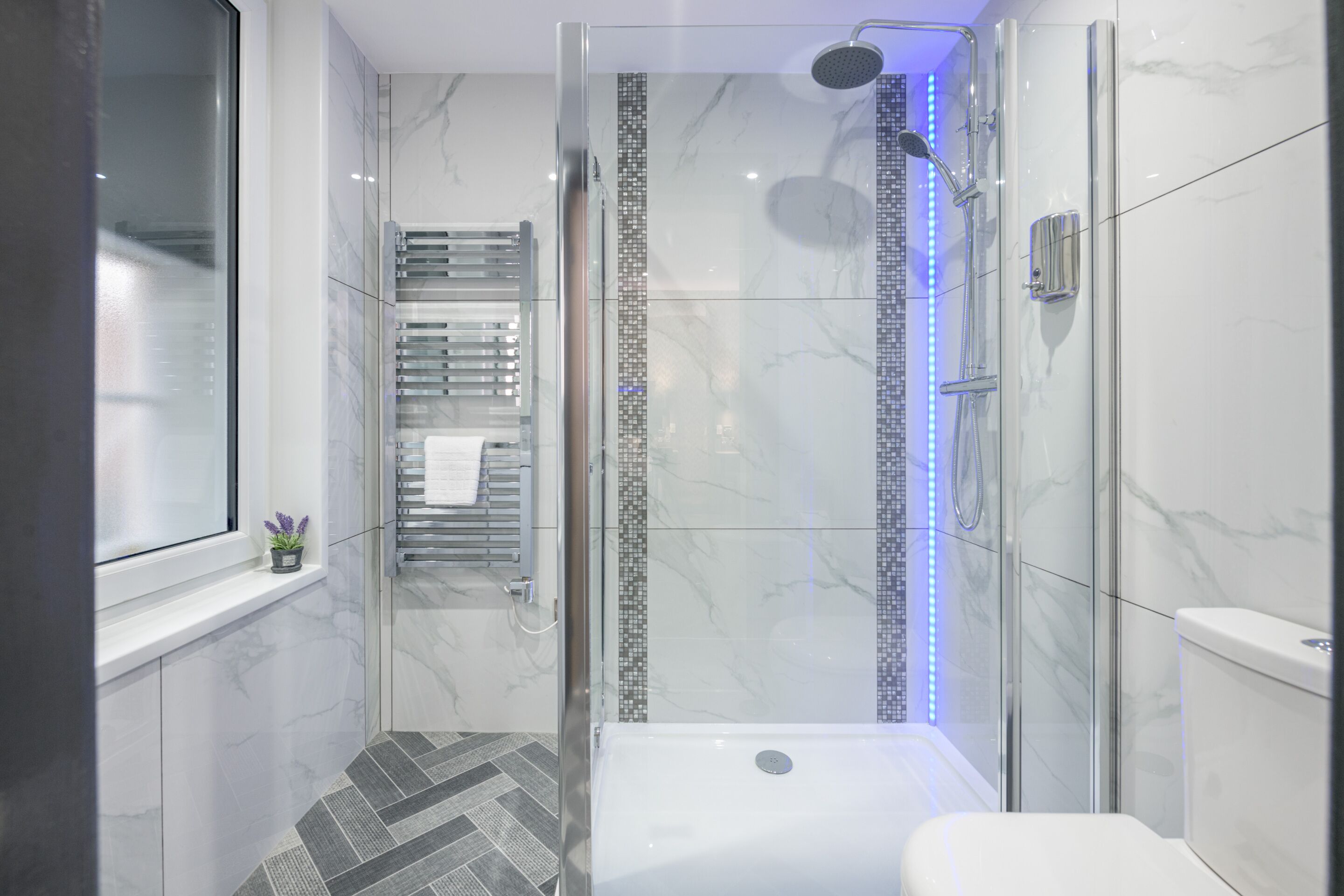 A modern bathroom with a glass-enclosed shower, a white bathtub, and a toilet.