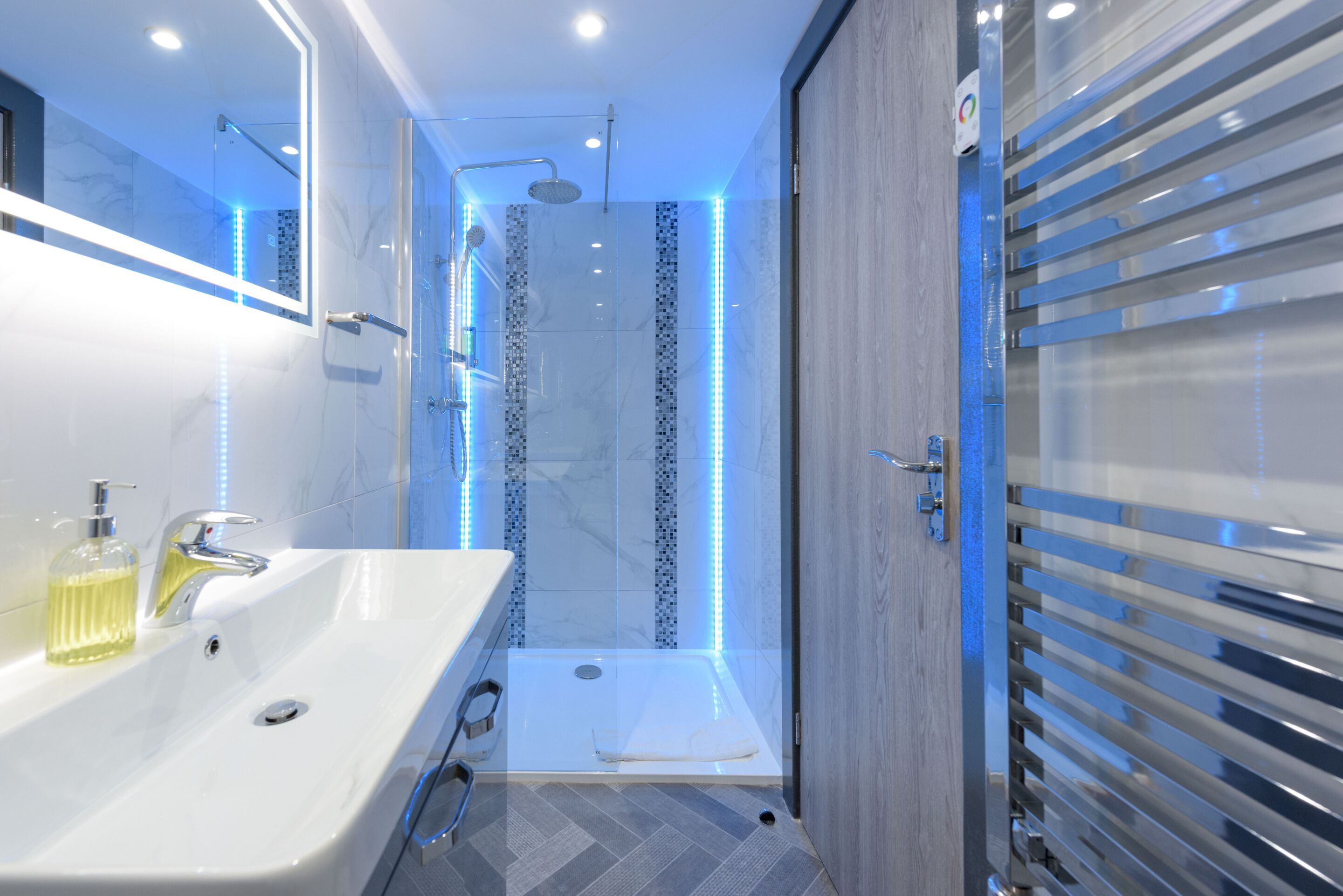 A modern bathroom with a large sink, a shower with LED lights, and a glass door.