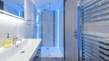 A modern bathroom with a large sink, a shower with LED lights, and a glass door.
