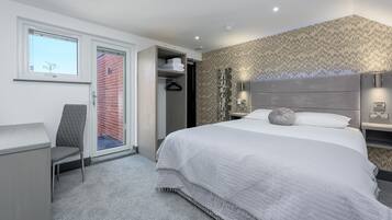 Habitación de hotel moderna con una cama grande, un escritorio, una silla, un armario y vista a un edificio de ladrillo a través de una puerta corredera.