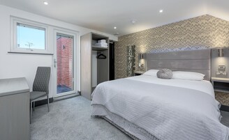Habitación de hotel moderna con una cama grande, un escritorio, una silla, un armario y vista a un edificio de ladrillo a través de una puerta corredera.