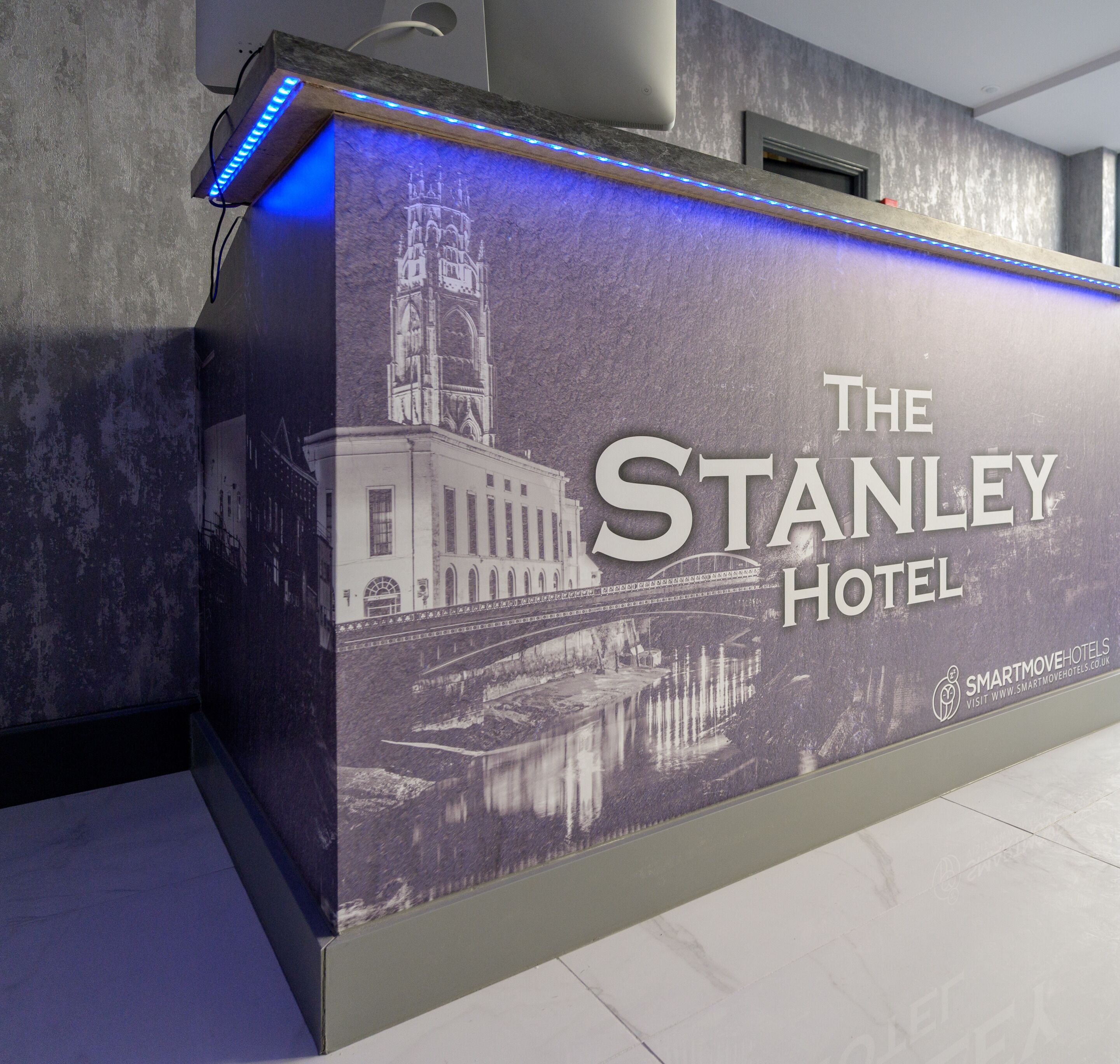 A reception desk with a large sign for The Stanley Hotel, featuring a historic building and a bridge reflection.