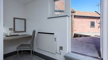 Una habitación con un radiador, una silla, una mesita, una ventana y vistas a un edificio de ladrillo.