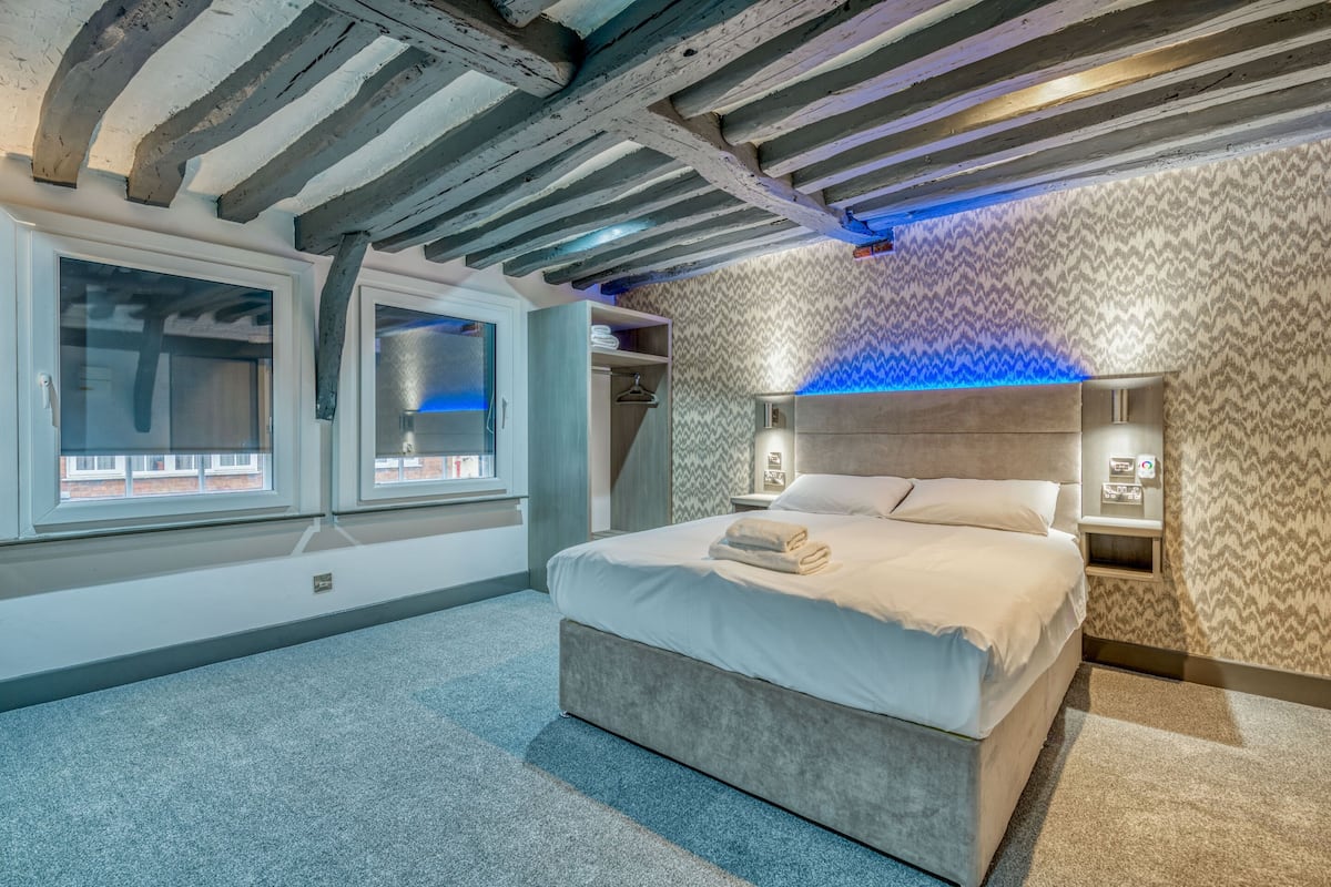 A modern bedroom with a large bed, a wooden ceiling, and patterned wallpaper.