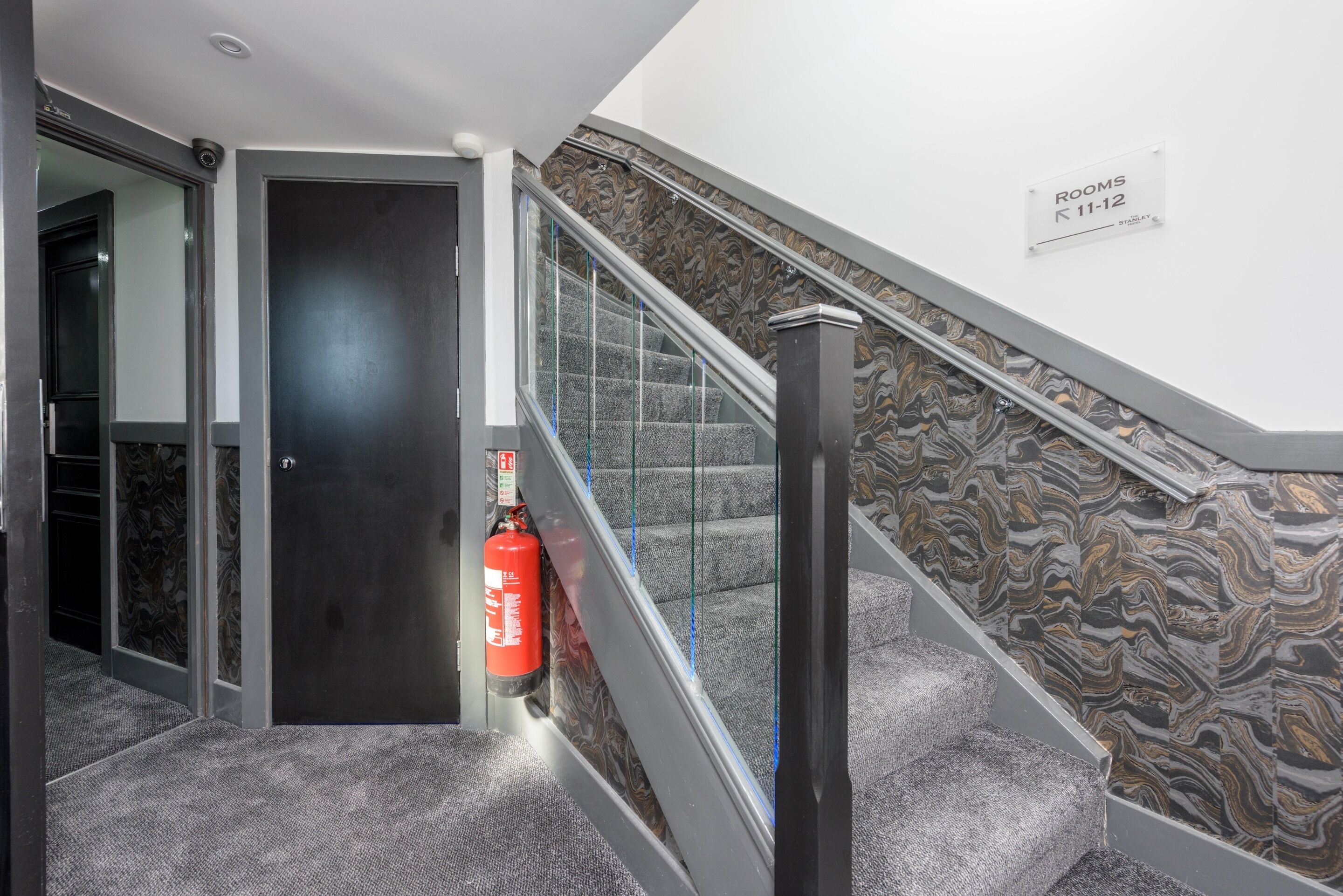 Una escalera con un revestimiento de pared con diseño de mármol, un extintor y un letrero que indica las habitaciones 11 y 12.