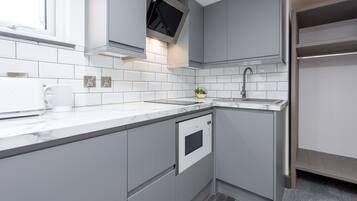 Una cocina moderna con armarios grises, horno empotrado, lavamanos y una ventana sobre la encimera.