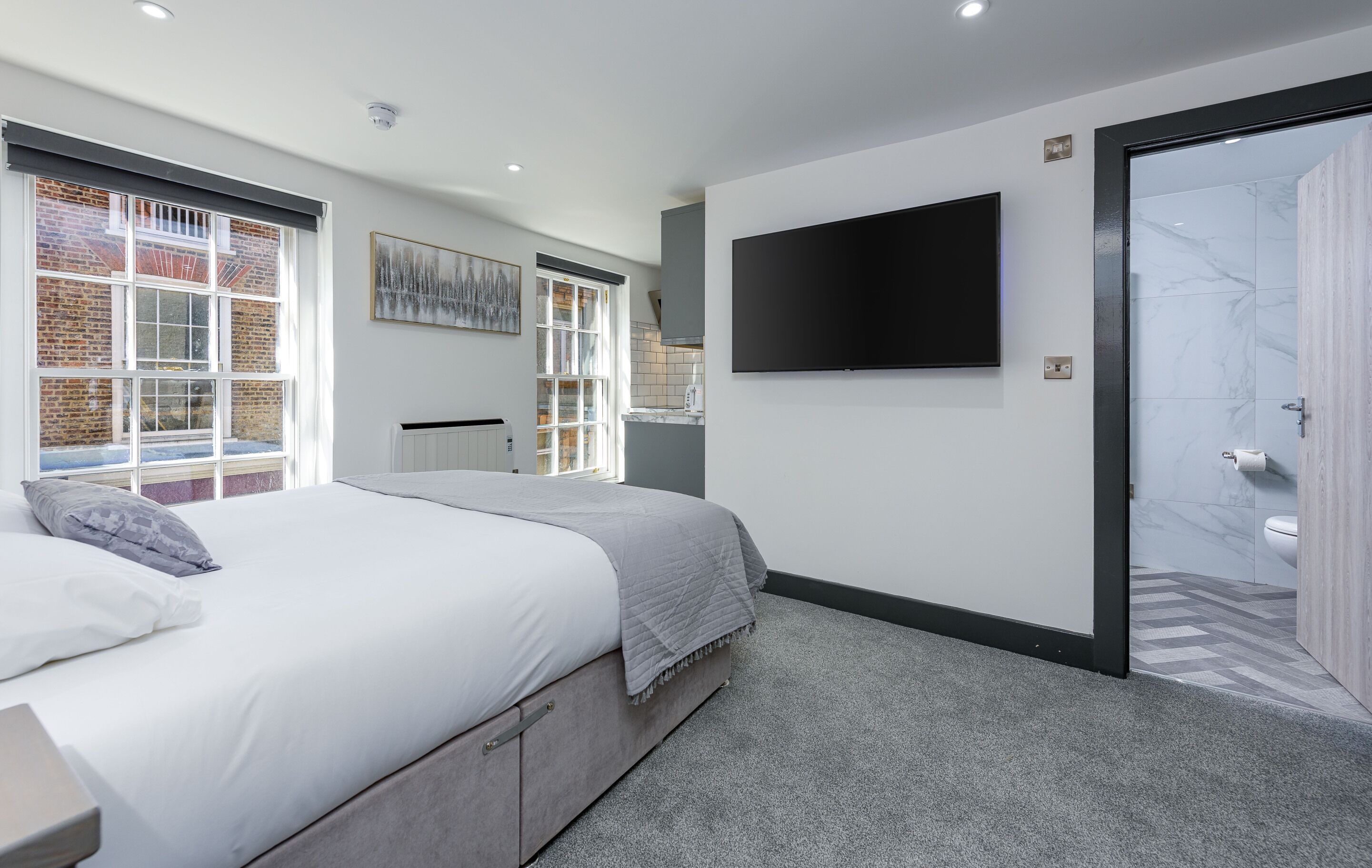 Un dormitorio moderno con una cama grande, un televisor montado en la pared y una puerta corrediza de vidrio que da a un baño.