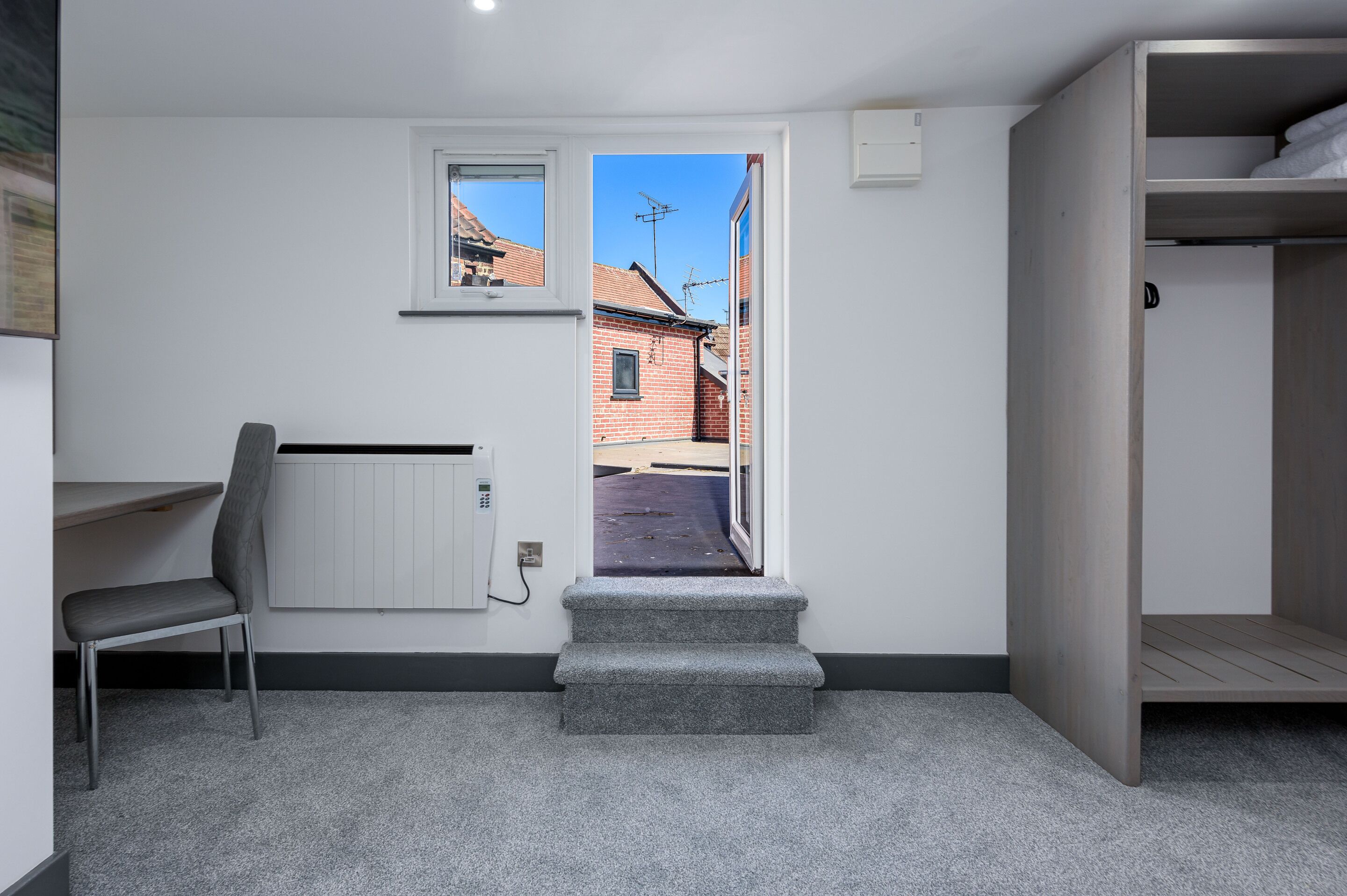 A room with a desk, chair, bunk bed, and a view of a street through a door.