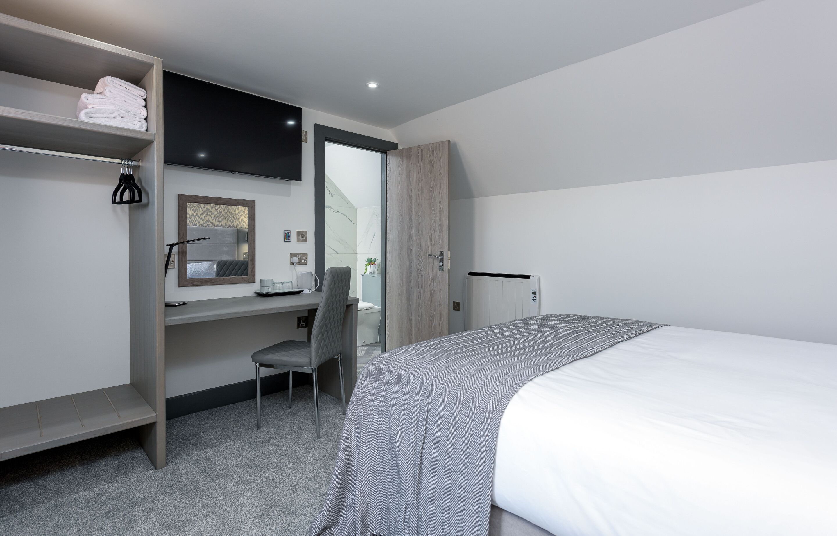 Et moderne hotelværelse med seng, skrivebord, stol, fjernsyn og garderobeskab.