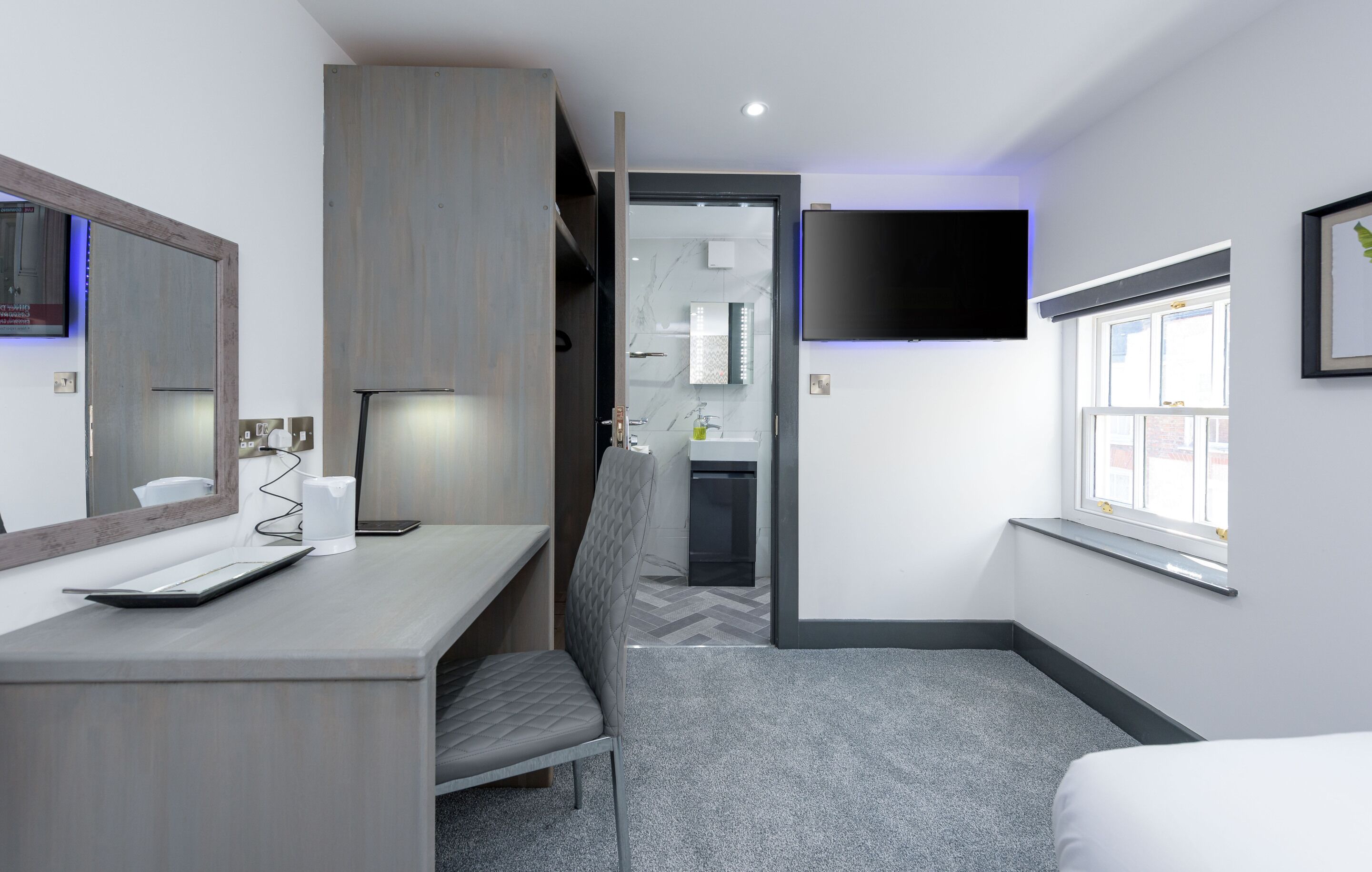 A hotel room with a desk, chair, bed, and a TV mounted on the wall.