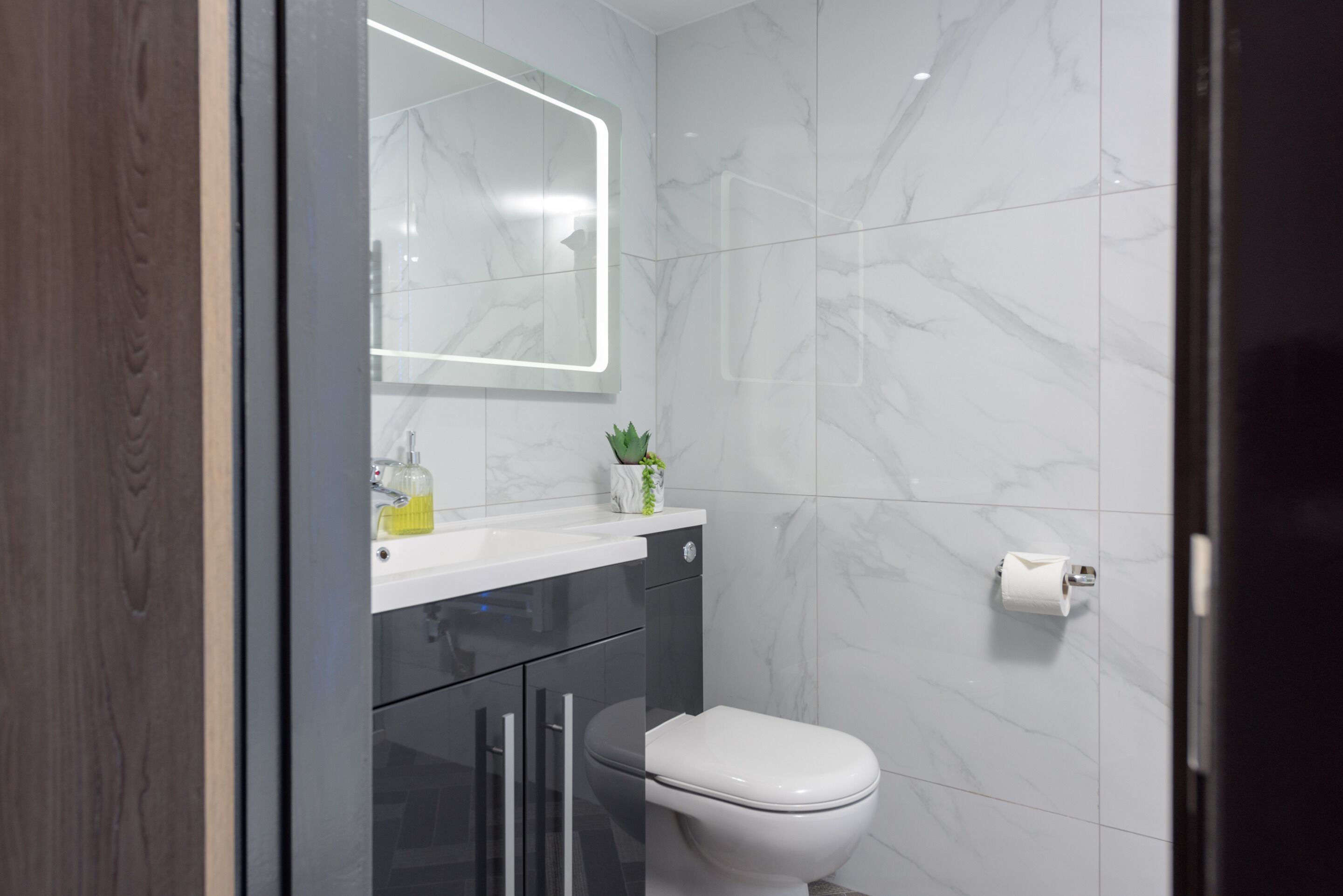 Een moderne badkamer met een toilet, een wastafel met spiegel en een wc-rolhouder.