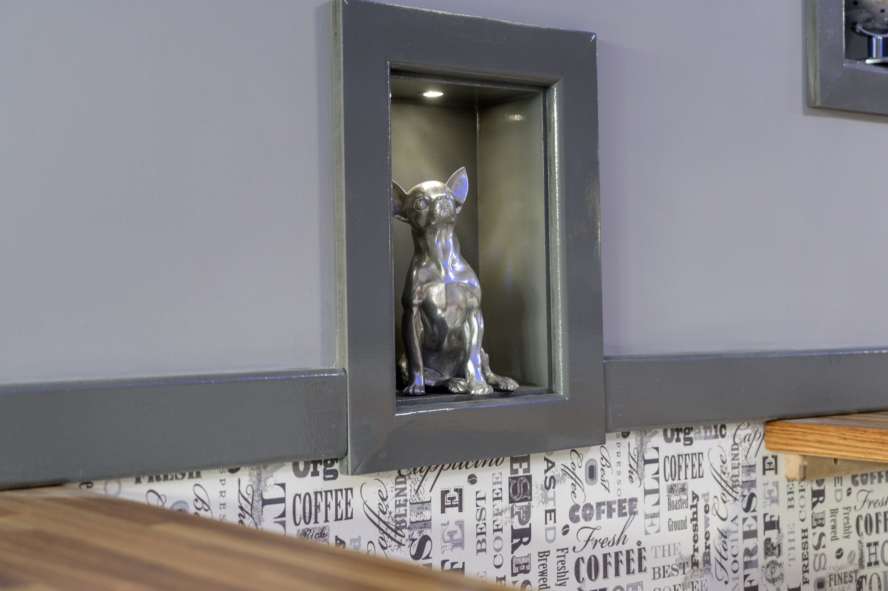 Una estatua de perro plateado en un nicho con marco en una pared con papel tapiz de temática de café.