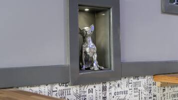 Una estàtua de gos daurat en un nínexe encastrat a la paret, amb paper pintat de temàtica cafè.