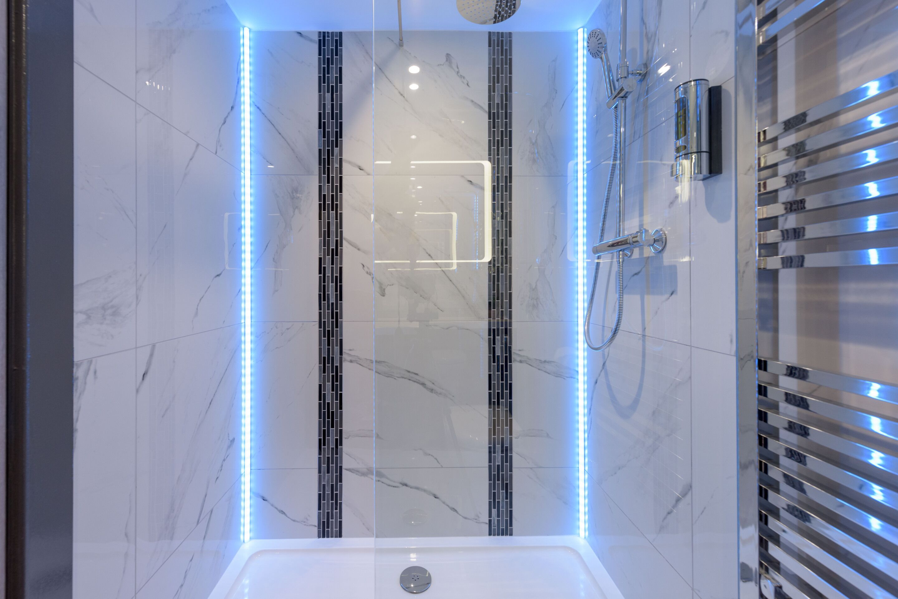 A modern bathroom with a glass-enclosed shower, marble tiles, and LED lighting.