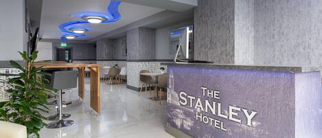 Un moderno hall de hotel con mostrador de recepción, zona de estar y un espejo grande.