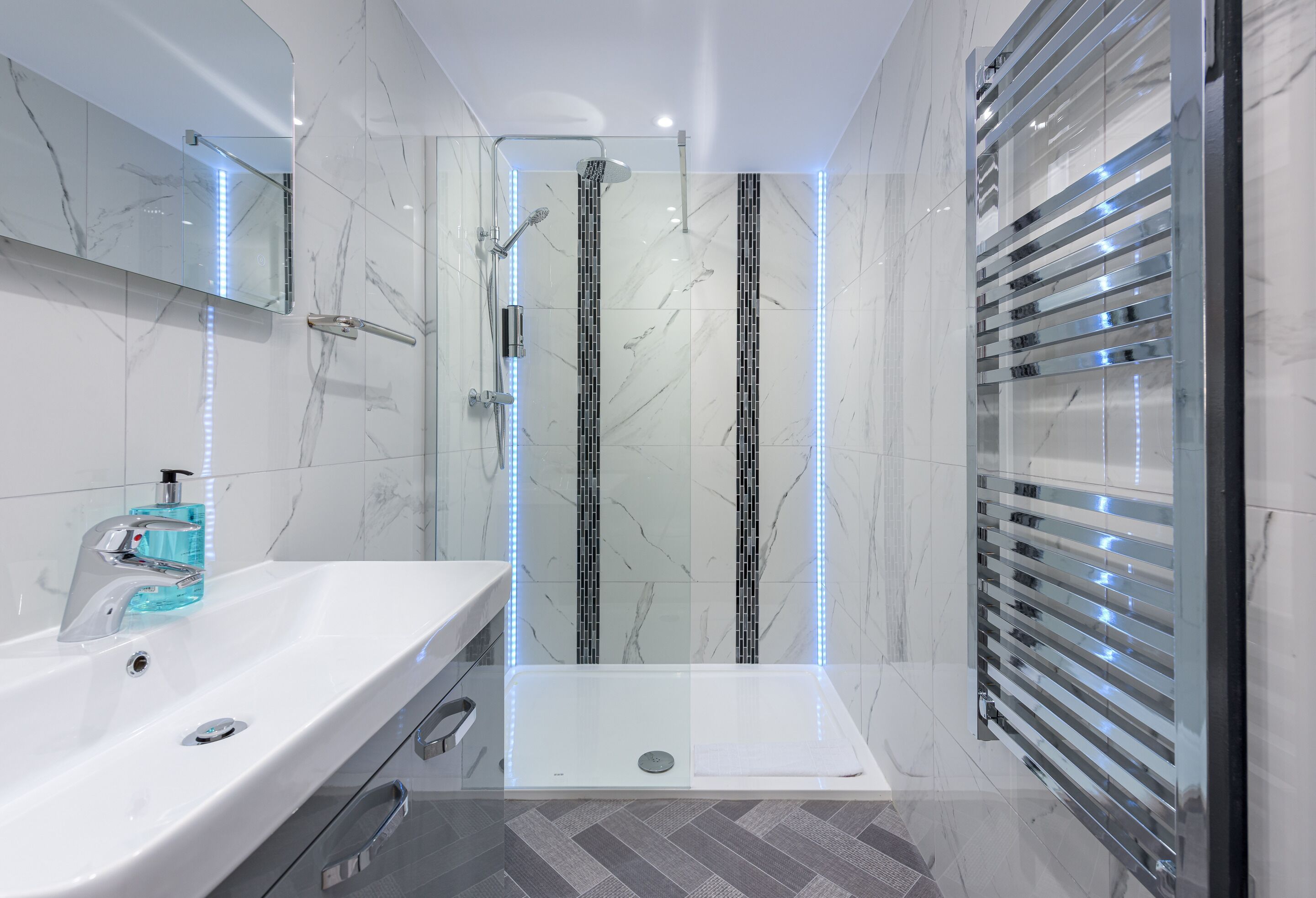 A modern bathroom with a glass-enclosed shower, a white sink with a soap dispenser, and a towel rack.
