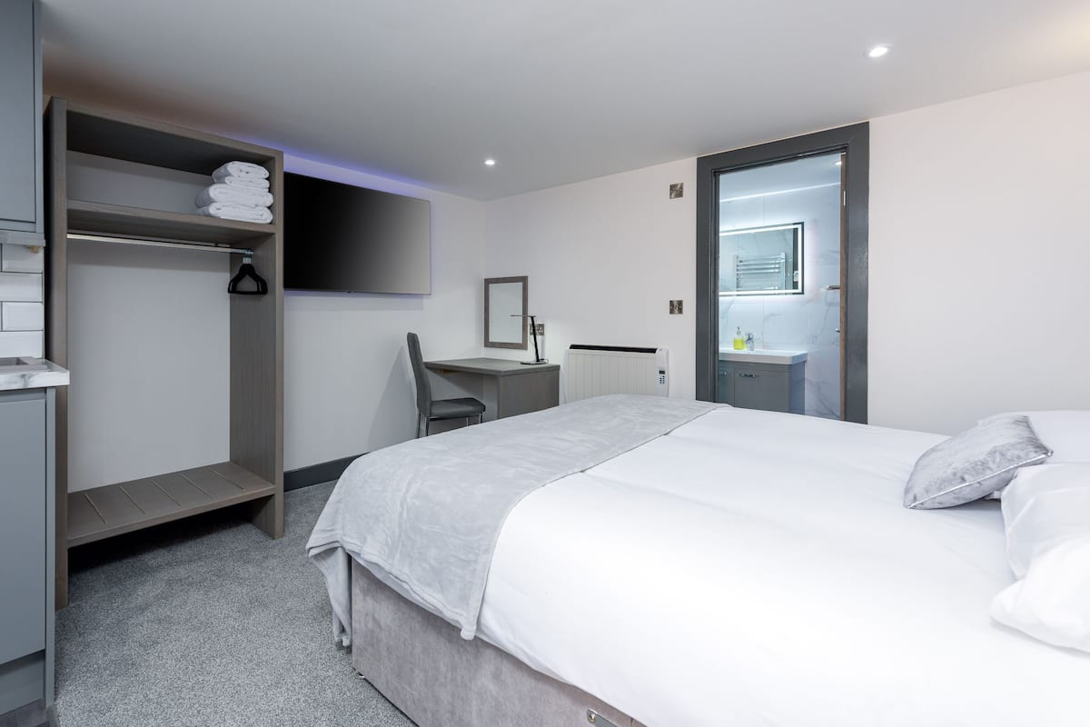 A modern hotel room with a bed, a desk, a chair, a wardrobe, and a bathroom.