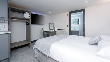 A modern hotel room with a bed, a desk, a chair, a wardrobe, and a bathroom.