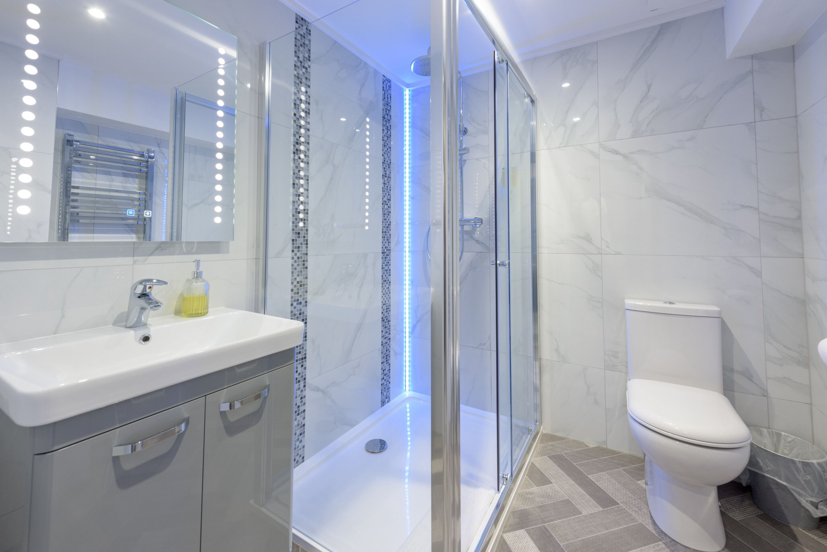 A modern bathroom with a glass-enclosed shower, a white sink with a mirror, and a toilet.