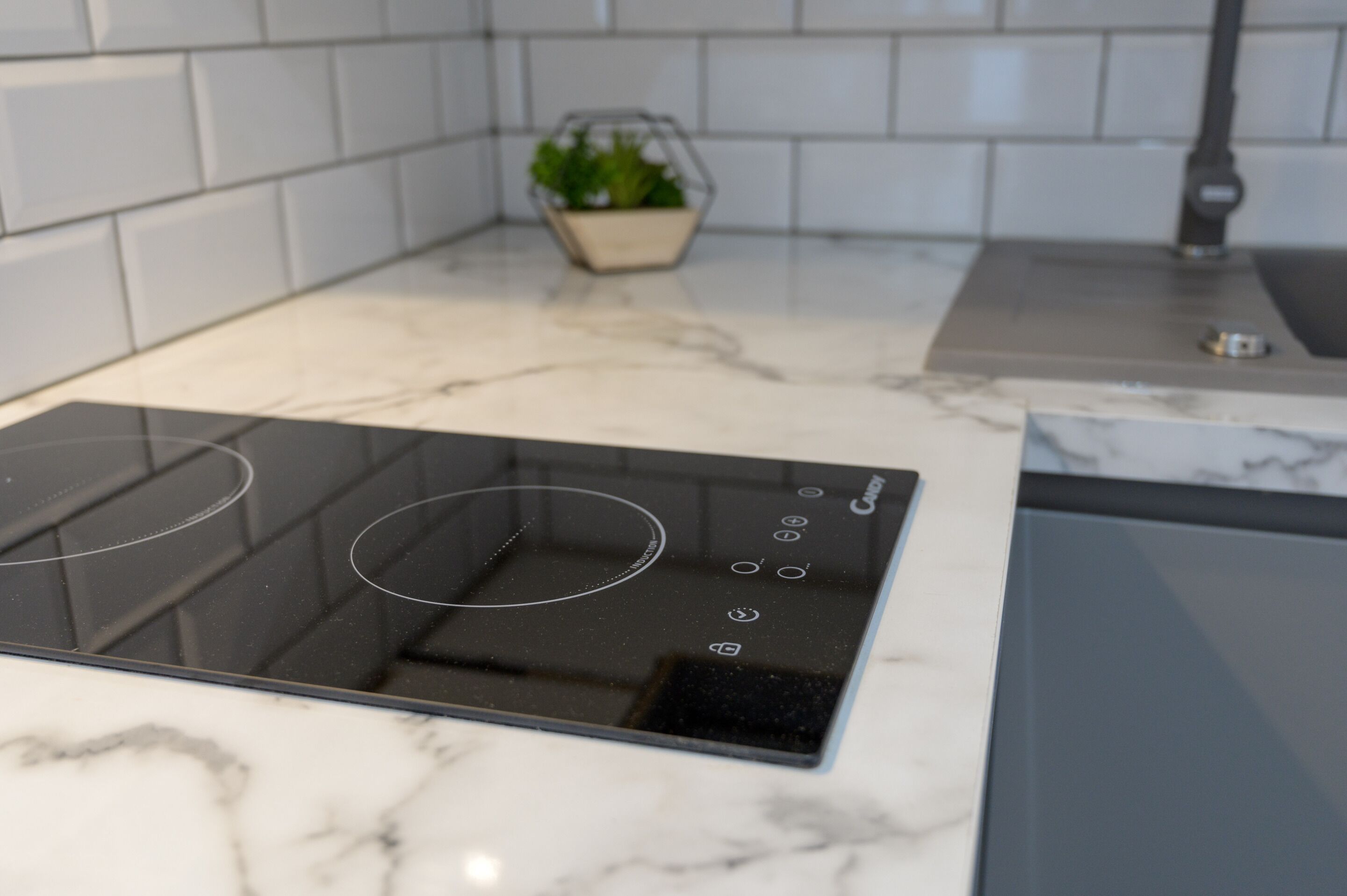 A kitchen with a black induction cooktop, white marble countertops, and a small potted plant on the counter.