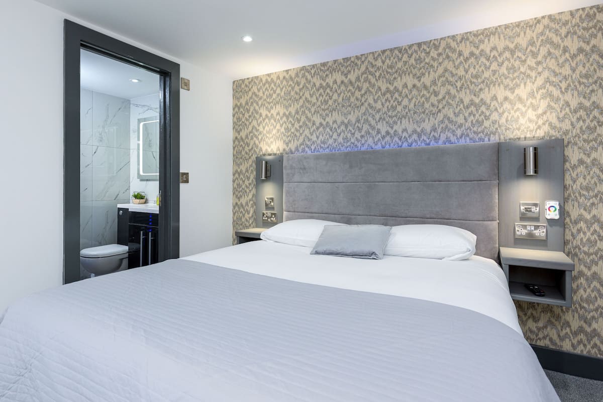 A modern hotel room with a large bed, a built-in vanity, and a shower area.