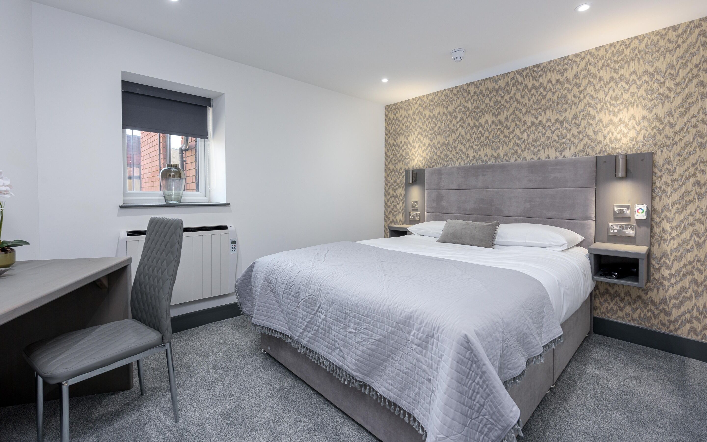 A modern hotel room with a large bed, a desk, and a chair.
