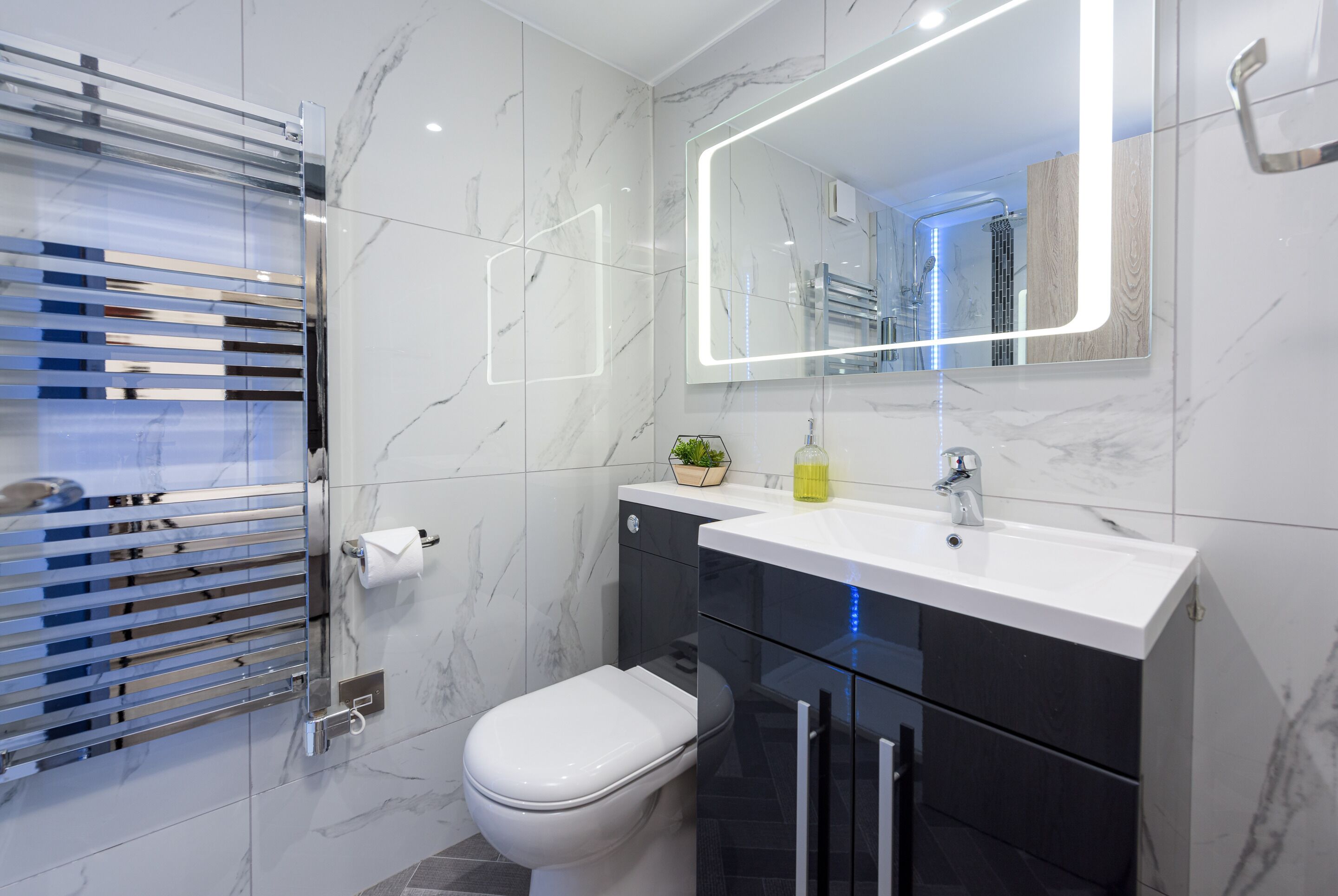 Un baño moderno con inodoro blanco, tocador negro y cabina de ducha con mampara de vidrio.