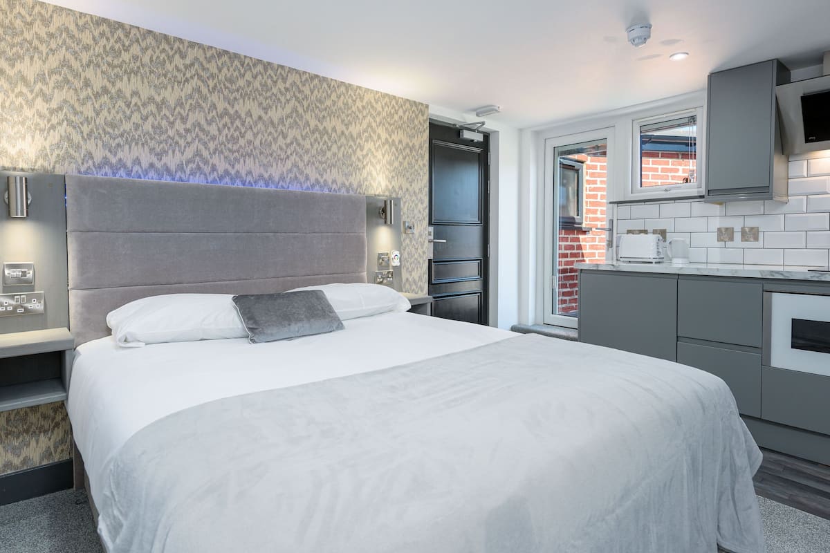 A modern hotel room with a large bed, a built-in desk, and a kitchenette.
