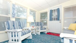 A room with a rocking chair, a chair, and a sofa with striped cushions. There is a door with a window and a sign that says "SWIM".