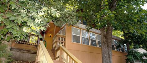A wooden staircase leading to a house with a large tree in front.