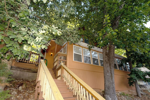 A wooden staircase leading to a house with a large tree in front.
