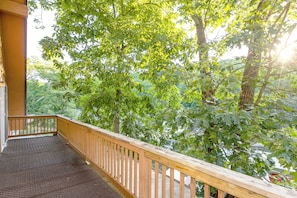 A wooden balcony with a metal safety grid, overlooking a lush green landscape with trees and a clear sky.