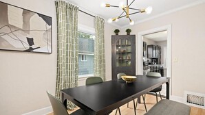 Comedor con una mesa de madera oscura, sillas verdes, un cuenco decorativo y una lámpara moderna.