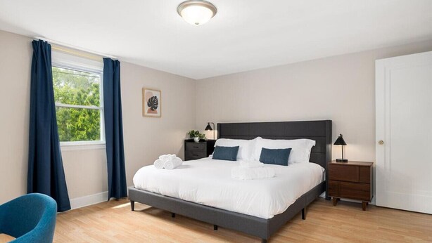Un dormitorio moderno con una cama grande, una mesita de noche, una silla y una ventana con cortinas.