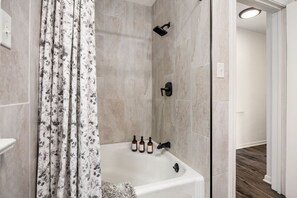 A bathroom with a bathtub, shower, and floral shower curtain. There are three bottles of shampoo on the edge of the tub. - Suburban Sanctuary: 3BD Perfect for Long Stays (Pekin)